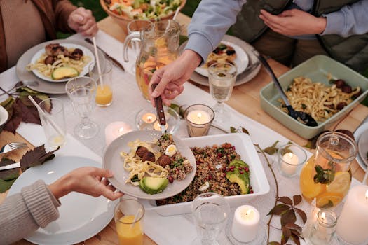 High angle of unrecognizable group of people eating together dinner with various dishes and drinks at table decorated with candles